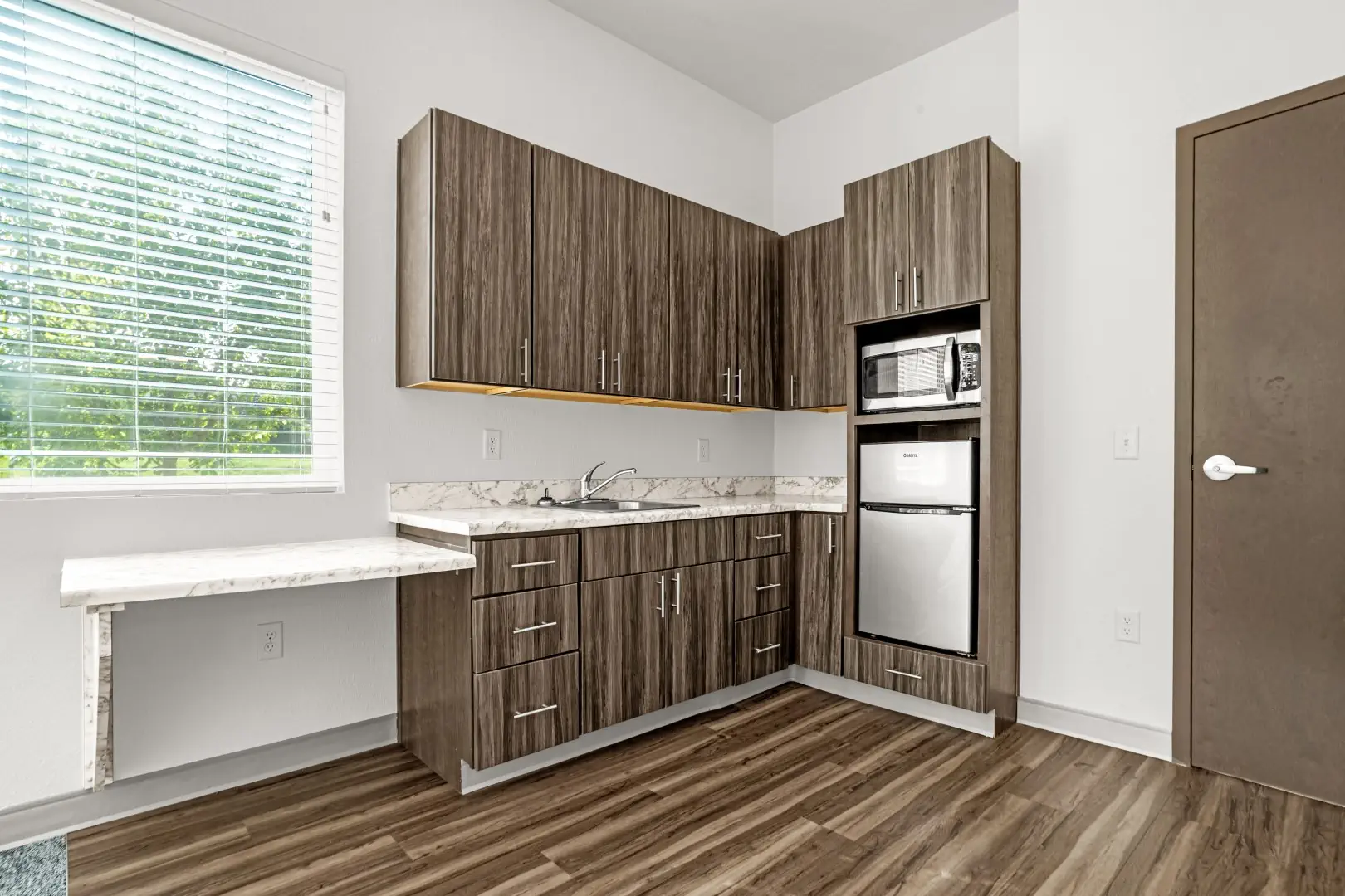 Kitchenette in studio apartment includes cabinetry, sink, refrigerator and microwave.